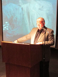 Terry Jude Miller stands at a lectern reading a poem to an audience.