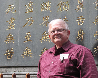 Terry smiles standing in front of a wall with carved Chinese calligraphic characters filled with gold.