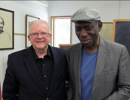 Terry Jude Miller & Yusef Komunyakaa smile and pose for a photo in business casual attire.